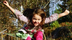 En leende flicka hoppar i skogen.