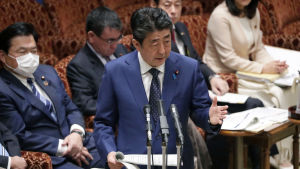 Japans premiärminister Shinzo Abe berättade att OS kan komma att flyttas fram under ett tal till det japanska parlamentet. Japans premiärminister Shinzo Abe står i ett talarpodie i Japans parlamet och håller tal om bland annat att sommar-OS i Tokyo kan komma att flyttas p.g.a coronapandemin. I bakgrunden sitter fyra personer, varav en bär ansiktsmask.