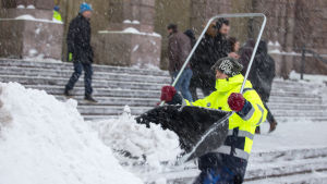 Mies heittää lunta lumikolalla Helsingin päärautatieasemalla.