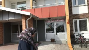 I en vanlig lägenhet i ett bostadshus i Rosengård har Yalla-trappan en lunchrestaurang. En kvinna med huvudduk går förbi ett bostadshus där det står Yalla-trappan ovanför dörren.