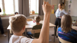 Det är viktigt att också prata om språk i en positiv bemärkelse i hemmet, påpekar Kurtén. Pojke räcker upp hand i klassrum