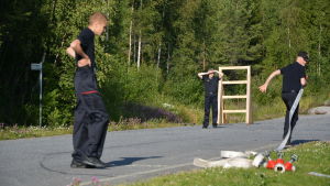 I tävlingen krävs precision, snabbhet och samarbete. En person springer med en brandslang medan två andra tittar på.
