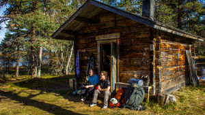 Kaksi retkeilijää istuu eräkämpän rappusilla Urho Kekkosen kansallispuistossa.