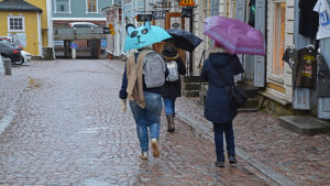 Vinterns trendaccessoar: paraplyet. Vädret är regningt och några människor går på en gata i Borgå gamla stad.