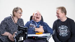Anneli Tuomi ja Taito Roivas katsovat keskellän pyörätuolissa istuvaa Seppo Viitasta. Kaikki kolme nauravat iloisena.