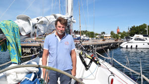 Olof Rytövaara är på sin andra seglingstur till Hangö den här sommaren. Man står på en segelbåt som är förtöjd vid en brygga i en hamn. I bakgrunden syns en stad. Staden är Hangö och vattentornet syns i bakgrunden.