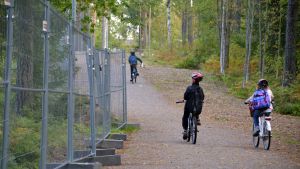 Bildningscentret är en byggplats omringad av staket i ännu en månads tid. Tre barn cyklar förbi Vårberga utbildningscentrum.