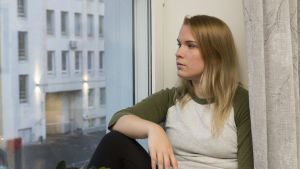 Sanna har lätt för att gå in i sin egen värld och spela roller för sig själv. Sanna Helander sitter på ett fönsterbräde och tittar ut genom fönstret.