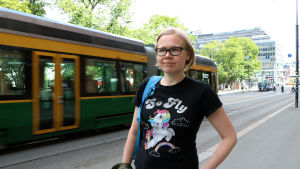 Fredrika Biström tycker det är trevligt att pride är en fest som engagerar många. Fredrika Biström står på trottoaren. Bakom henne kör en spårvagn.