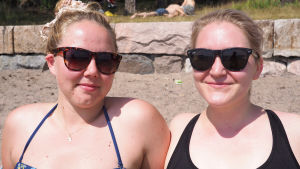 Hanne Rainesalo (t.v.) och Isabella Vilkman njuter av solen på Blåbärslandet i Helsingfors, men tänker inte svalka sig i vattnet bland de blågröna algerna. Hanne och Isabella solar på en sandstrand i Helsingfors