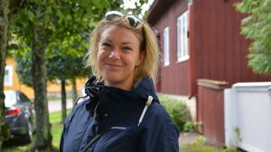 Ida Arnold-Larsen är uppvuxen i Lovisa men bor numera på annat håll. Kvinna ler vid ett gammalt rött trähus.
