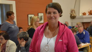 Lilian Järvinen var en diskussionsmötets arrangörer. Kvinna står och ler bland människor som dricker kaffe och äter kaka.
