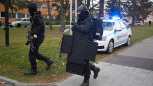 På plats finns både den lokala polisen och polisens specialstyrka. Gärningsmannen söks nu med hjälp av helikopter. Svartklädda poliser med skyddsvästar springer.