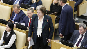 Valentina Teresjkova står bland bänkrader där människor sitter. Hon har brunt hår med en grå hårrand som går från pannan och bakåt över huvudet och bär en mörkt blågrönrutig kavaj.