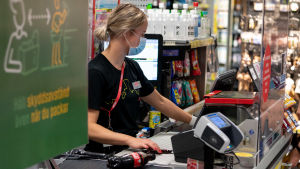 Det skadar inte att använda munskydd även om det finns tillexempel en plexiskyddsskiva i butikens kassa. Salen myyjä palvelee asiakasta maski päässään.