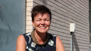 Projektledaren Annette Kronholm-Cederberg. En kvinna med kort mörkt hår kisar. Bakom henne syns en grå tegelvägg.