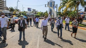 Journalister demonstrerade på en av huvudgatorna i Acapulco i delstaten Guerrero i Mexiko, efter mordet på journalisten Victor Álvarez Chávez, i april. Álvarez hittades styckad efter att han försvunnit den 2 april. Personer med munskydd går på en asfalterad gata i solskenet, med blå himmel i bakgrunden och en stor, grön palm på sidan av vägen.