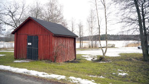 Den här byggnaden lovar staden avlägsna och i bakgrunden syns bryggan som företaget får rätt att förnya. En röd, mindre byggnad som står på en gräsmatta i närheten av vattnet.