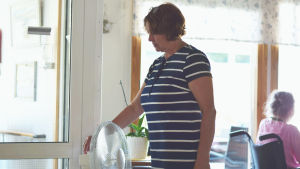 Camilla Biström lägger på en av fläktarna på Lönneberga. Kvinna i randig klänning lägger på fläkt inomhus. I Bakgrnden en äldre kvinna i rullstol.