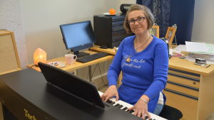 Sångpedagogen Pia Lindvall. En leende kvinna sitter vid ett piano och tittar in i kameran.