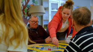 Yrjö Toivola och Tove Hammarström spelar tillsammans. Tove flyttar en röd kimble knapp, en äldre man vid bordet ser på.