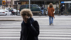 Telefonskräck kan handla om att det är jobbigt att både ringa och svara på samtal. Nainen puhuu puelimessa ja ylittää tietä etualalla. Takana toinen nainen ja kaksi pyöräilijää.