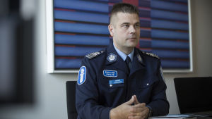 Kimmo Ulkuniemi jobbar som polisinspektör inom cyber- och it-brottslighet. En medelåldersman i polisuniform sitter vid ett bord med knäppta händer.