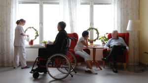 Inom äldreomsorgen skulle det behövas fler arbetstagare. Bild: Mostphotos Två personer sitter i var sin fåtölj och samtalar. På bilden finns också en person i rullstol och en person som står vid ett fönster och vattnar en växt.