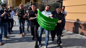 En anhängare som demonstrerade sitt stöd för Golunov, leds bort av poliser En demonstrant med ett grönt plakat med text på ryska leds bort av två poliser