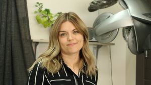 Sara Mäkelä är orolig för de ekonomiska följderna. En kvinna med långt ganska ljust hår står inne i en frisörsalong.