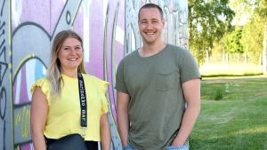 "Jag brukar säga att jag har ett bultande Karishjärta fastän jag har flyttat bort härifrån", säger producent Elin Sundell. Här tillsammans med projektkollegan och kompisen Ian Granström. Producent Elin Sundell i gul t-skjorta och fotograf Ian Granström i grönt. De står framför en vägg med grafitti i lila färger.