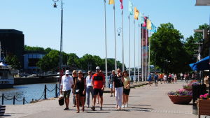 Övervakarna har rört sig kring uteserveringarna vid ån för att kontrollera restriktioner. Människor promenerar längs med Aura å i sommarsolen.