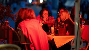 Inga alkoholdrycker får säljas mellan klockan 23 och 06 på grund av coronaviruset på många håll i Estland. Bilden är från Tallinn och tagen i juni 2020. Ett gäng kvinnor sitter på en uteservering på kvällen och dricker en och samma stora dryck ur sugrör. Det lyser ett rött sken på kvinnorna.