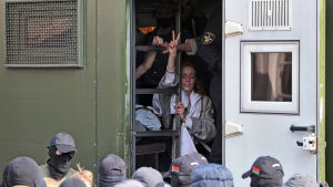 Polisen skuffade in demonstranter i sina transportfordon. Genom dörren till ett polisfordon syns en kvinna som visar peace-tecknet.