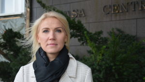 Direktören för Vasa sjukvårdsdistrikt Marina Kinnunen säger att vårdanställda har lärt sig bli betydligt noggrannare med att inte komma till jobbet med symptom, det kan man lära sig också inom annan verksamhet. Marina Kinnunen, en vit kvinna med blont hår, står utanför Vasa centralsjukhus.