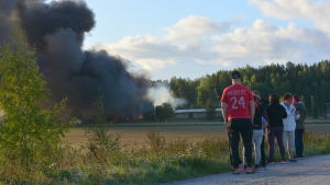 Evakuerade Salobor står och tittar på branden. Personer som står med ryggen mot kameran och ser på en fabrik som brinner.
