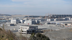 Flygplatsen Istanbul Airport har fått sitt namn efter staden Istanbul, vars namn också är ett viktigt varumärke för landet, sade president Erdogan under invigningen. En bild på ett flygfält. På bilden syns gråa byggnader och platt, sandigt landskap.