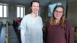 Karin Kastrén och Nina Martin Två unga kvinnor i skolsal med stolar och bioduk längst fram. En ena kvinnarn ler stort och den andra ser underfundig ut. Den ena är klädd i ljusa kläder och den andra i mörkt