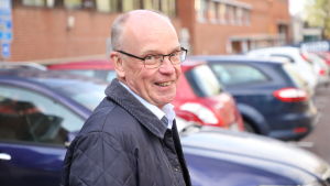 Nils-Olof Nylund gläder sig åt att det kommer ut många eldrivna familjebilar på marknaden, även om priserna är höga. En leende äldre man utomhus. Han har glasögon och blå jacka och många bilar i bakgrunden.