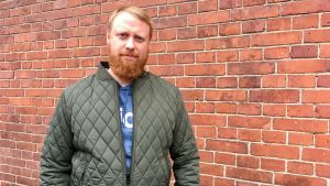 Sami Salmivirta. Sami Salmivirta poserar utomhus framför en röd tegelvägg.