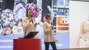 Anne Kuutio (t.v.) och Laura Oksanen höll föräldrarnas anförande under mötet. Två kvinnor håller ett föredrag framför en skärm. De ser ivriga ut. På skärmen syns bilder på barn som leker.