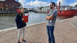 Det här var första gången som Aho höll en guidning för bara en turist. Resultatet blev en lite mera personlig guidning. Maria Aho står med ett rött paraply och en röd mapp och berättar.