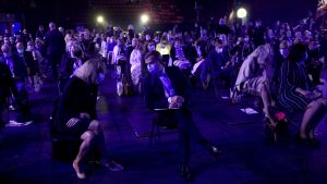 Coronatidens Samlingspartister, med munskydd, på partikongress i Björneborg En grupp mötesdeltagare med munskydd sitter glest i blått upplyst mötessal.