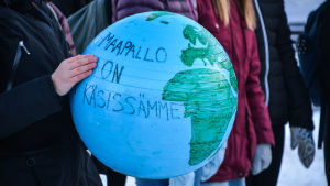 "Jordklotet är i våra händer" står det på en boll som en av gymnasieeleverna i Borgå hade med sig till torget. Närbild på en gympaboll som har målats till en jordglob. Någon står utomhus och håller i den.