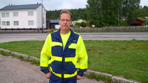 Dennis Björklund. En man med neongul jacka står framför en gräsplätt och en väg.