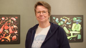 Johanna Sandin med några av sina konstverk. En kvinna står framför två fototavlor med plastskräp. Den ena tavlan har rött plastskräp, den andra grönt. Väldigt vackra tavlor.