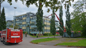 Brandpersonal hissades upp för att kunna släcka branden. Våningshus och brandbilar.