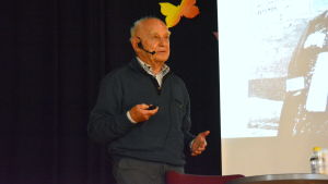 Piotr Zettinger besöker drygt 20 skolor per år. Bilden är från S:t Olofsskolan i Åbo där han i oktober 2019 föreläste för 250 åttonde- och niondeklassare. en äldre man föreläser, i bakgrunden syns en del av hans skärm