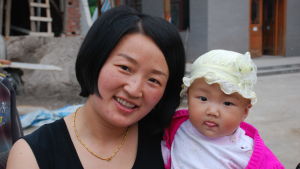 Det är vanligt att föräldrar väljer att inte göra ett andra barn. De har själva vuxit upp som enda barn. En kinesisk mamma och hennes dotter. Mamman har page, svart topp och ett guldsmycke. Flickan är ännu ett spädbarn och klädd i en ljusgul hatt. Hon sträcker ut tungan.