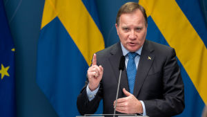"Det är självklart så att vi alla önskar ett datum där vi kan återgå till hur det var innan det här. Men det här är helt beroende av verkligheten och hur belastad sjukvården är", sa statsminister Stefan Löfven. Stefan Löfven på pressträff framför svenska flaggor, med pekfingret höjt i förmaning.